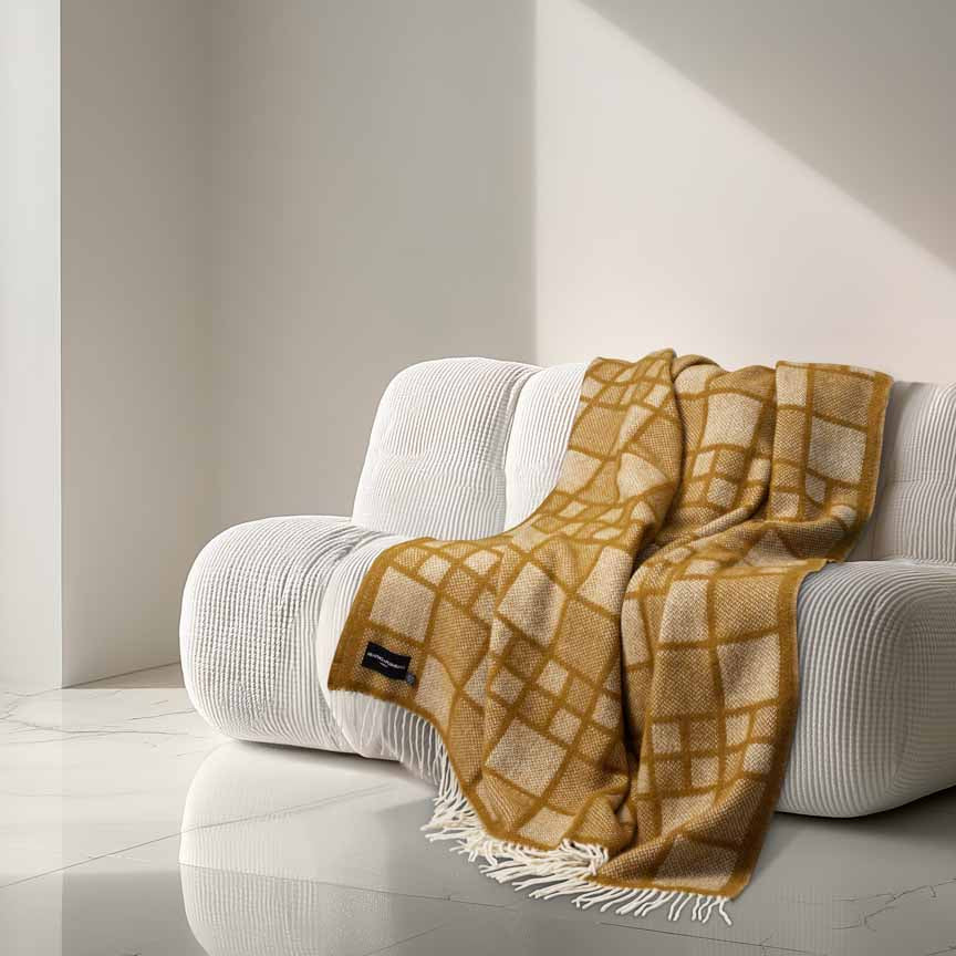 Heating & Plumbing London Mosaic Toffee checked wool throw draped over a curved cream sofa in a minimalist, AI-generated modern interior with marble flooring and soft directional light.
