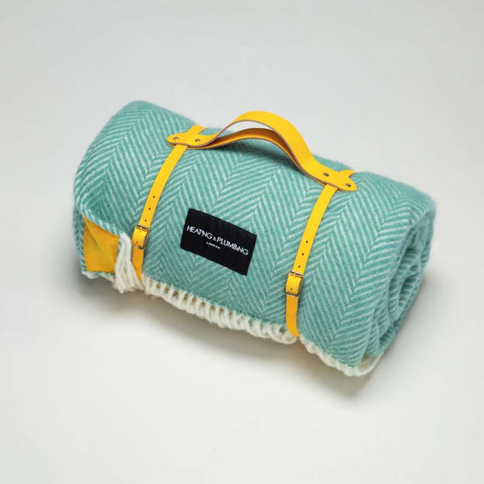 Mint green picnic blanket in wool with a yellow waterproof backing and a yellow leather strap