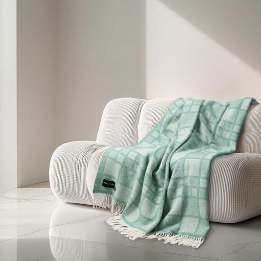 Heating & Plumbing London 'Mosaic Mint' checked wool throw draped over a curved cream sofa in a minimalist, AI-generated modern interior with marble flooring and natural directional light. 864