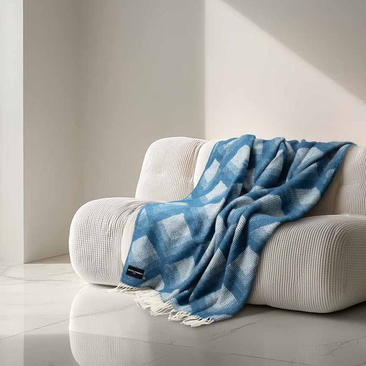 Heating & Plumbing London Swinging London blue and white checked wool throw draped over a curved cream sofa in a minimalist, AI-generated interior with marble flooring and soft natural light. 864